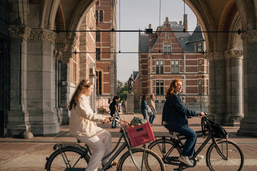 Two friends cycle through the Rijksmuseum into Museumplein in Amsterdam